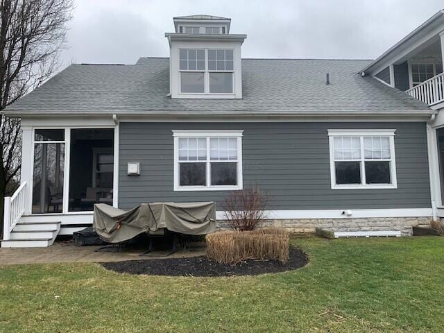 back of property featuring entry steps, roof with shingles, and a lawn