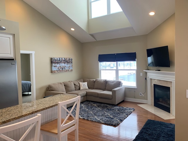 living room with high vaulted ceiling, light wood-style flooring, recessed lighting, a high end fireplace, and baseboards