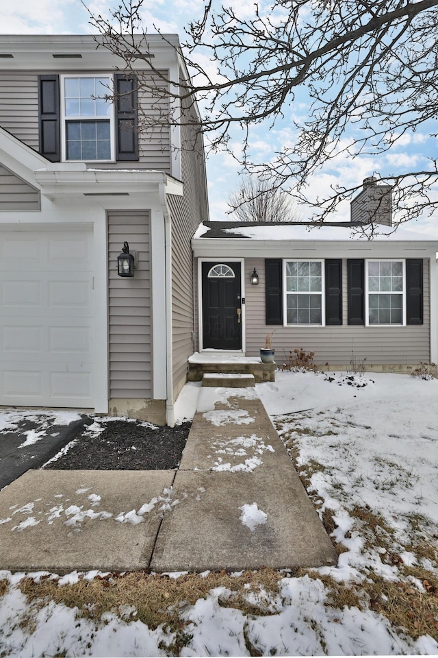 snow covered property entrance featuring a garage and a chimney