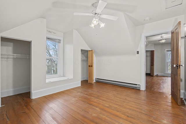 unfurnished bedroom featuring vaulted ceiling, a baseboard radiator, hardwood / wood-style flooring, ceiling fan, and multiple closets