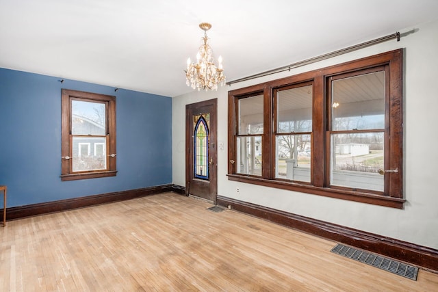 unfurnished room with a notable chandelier, a wealth of natural light, and light wood-type flooring