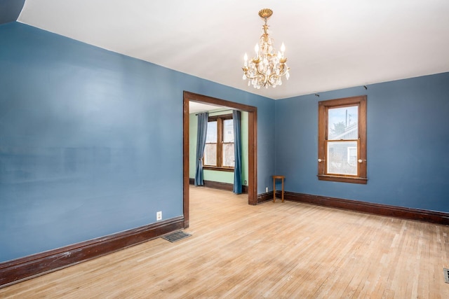 empty room with light hardwood / wood-style floors and a notable chandelier