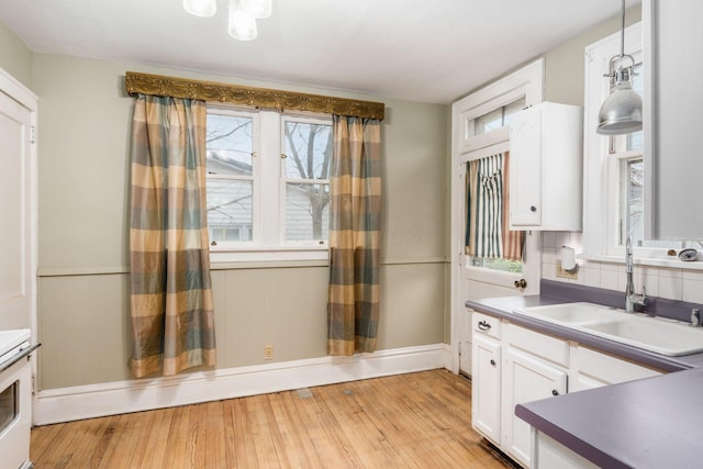 kitchen with white cabinetry, sink, backsplash, hanging light fixtures, and light hardwood / wood-style flooring