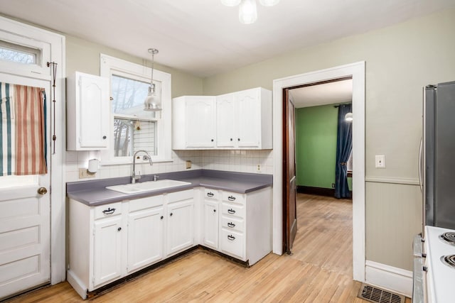 kitchen with decorative light fixtures, white cabinetry, sink, stainless steel fridge, and light wood-type flooring