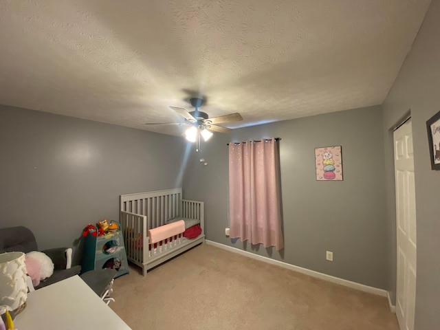 bedroom featuring a textured ceiling, a crib, light colored carpet, and ceiling fan