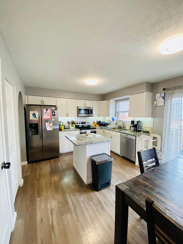 kitchen with a kitchen island, sink, white cabinets, stainless steel appliances, and light wood-type flooring