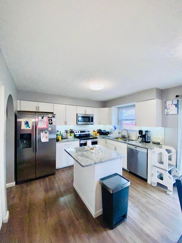 kitchen featuring sink, appliances with stainless steel finishes, hardwood / wood-style floors, a center island, and white cabinets