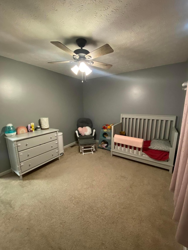 carpeted bedroom with ceiling fan, a crib, and a textured ceiling