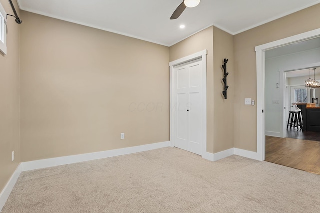 unfurnished bedroom with ornamental molding, carpet floors, ceiling fan with notable chandelier, and a closet