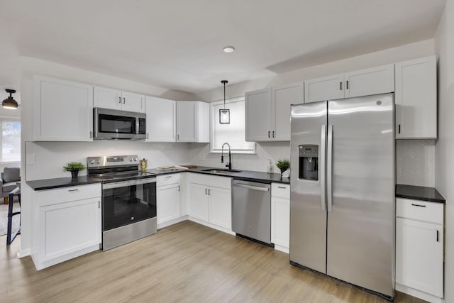 kitchen featuring pendant lighting, sink, white cabinets, stainless steel appliances, and light hardwood / wood-style flooring