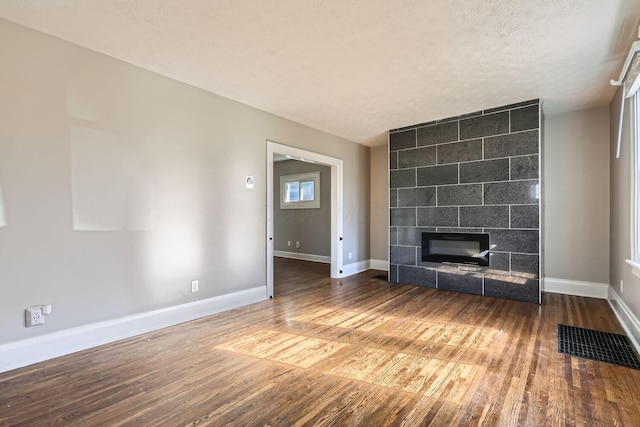 unfurnished living room featuring hardwood / wood-style flooring, a textured ceiling, and a tiled fireplace