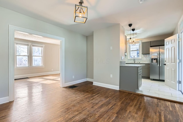 kitchen featuring gray cabinetry, stainless steel refrigerator with ice dispenser, decorative light fixtures, light hardwood / wood-style floors, and a wealth of natural light