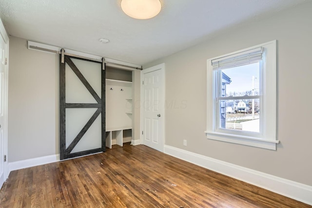 unfurnished bedroom with dark hardwood / wood-style floors and a barn door