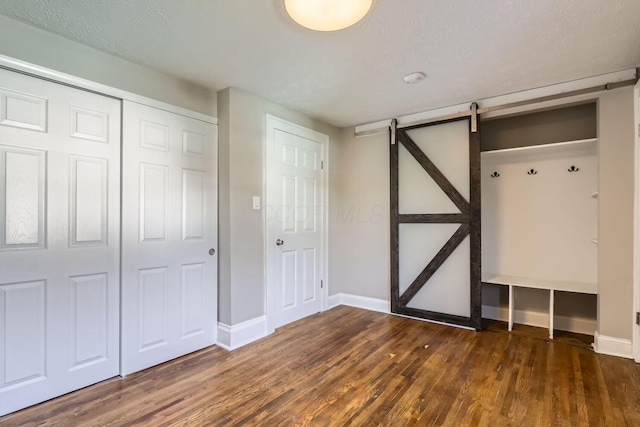 unfurnished bedroom with a closet, dark wood-type flooring, a barn door, and a textured ceiling