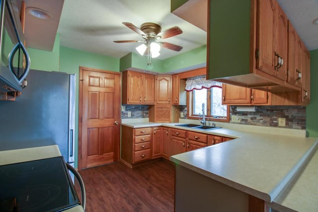 kitchen with dark wood-type flooring, sink, appliances with stainless steel finishes, kitchen peninsula, and decorative backsplash