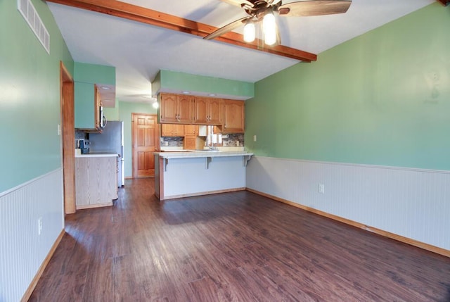 kitchen featuring beamed ceiling, ceiling fan, a kitchen bar, and kitchen peninsula