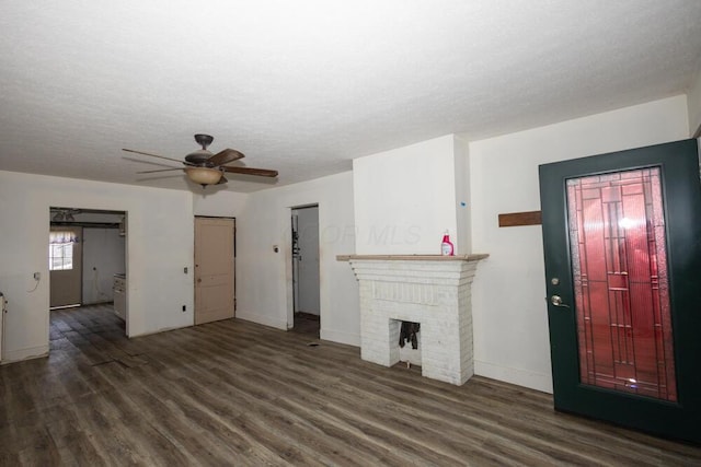 unfurnished living room featuring dark wood-type flooring, ceiling fan, a brick fireplace, and a textured ceiling