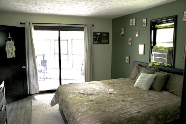 bedroom with hardwood / wood-style floors, access to exterior, a textured ceiling, and cooling unit