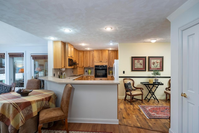 kitchen featuring dark hardwood / wood-style floors, black appliances, sink, kitchen peninsula, and a textured ceiling