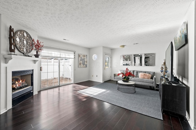 living room with dark wood-type flooring, a tile fireplace, and a textured ceiling