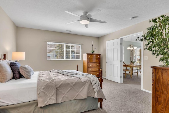 bedroom with visible vents, ceiling fan with notable chandelier, a textured ceiling, baseboards, and light colored carpet