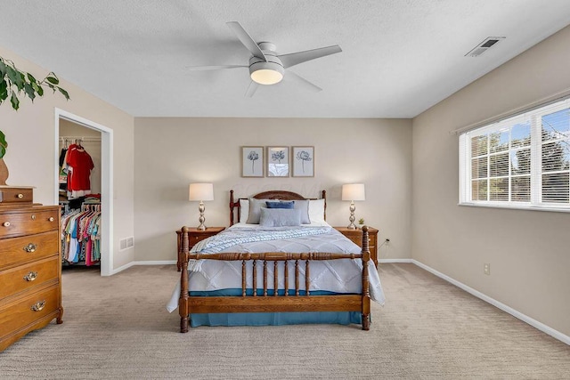 carpeted bedroom featuring a closet, visible vents, a textured ceiling, and a walk in closet