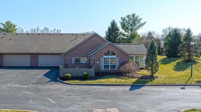 view of front of house with aphalt driveway, an attached garage, brick siding, and a front lawn