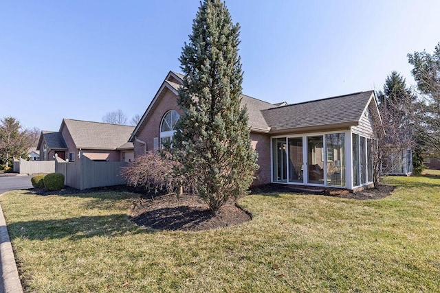 view of side of home featuring a yard, fence, a shingled roof, and a sunroom