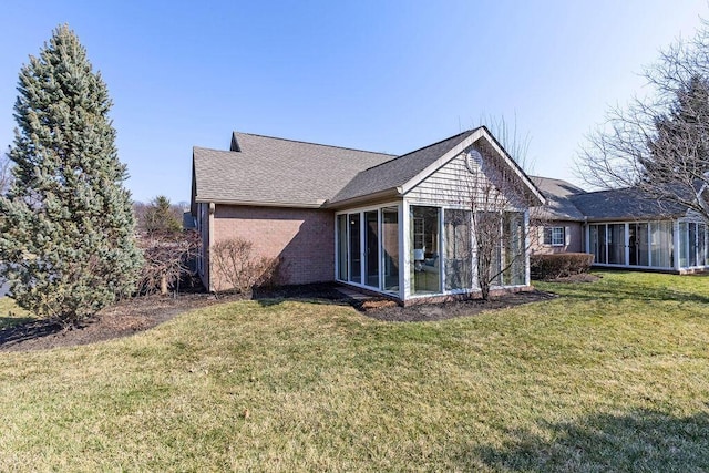 view of home's exterior with a lawn, brick siding, a sunroom, and roof with shingles