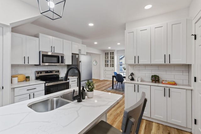 kitchen with light wood-type flooring, light stone countertops, white cabinets, and appliances with stainless steel finishes