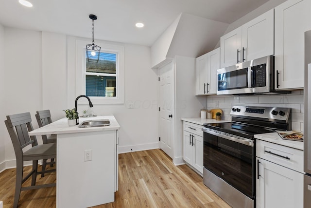 kitchen with sink, white cabinetry, decorative light fixtures, appliances with stainless steel finishes, and a kitchen breakfast bar