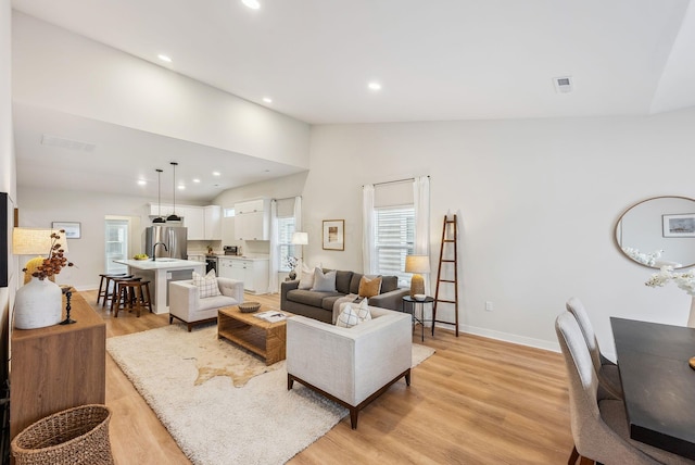 living room featuring vaulted ceiling, sink, and light hardwood / wood-style flooring