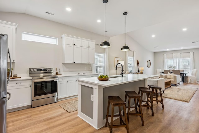 kitchen featuring lofted ceiling, pendant lighting, stainless steel appliances, a kitchen island with sink, and white cabinets