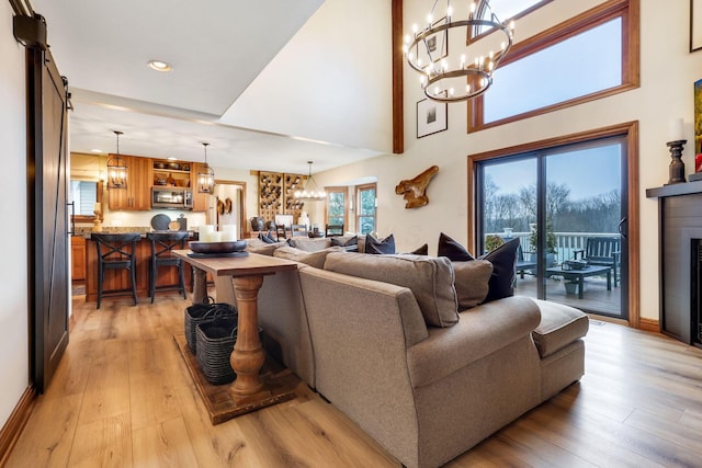 living room featuring a barn door, a towering ceiling, an inviting chandelier, and light hardwood / wood-style floors