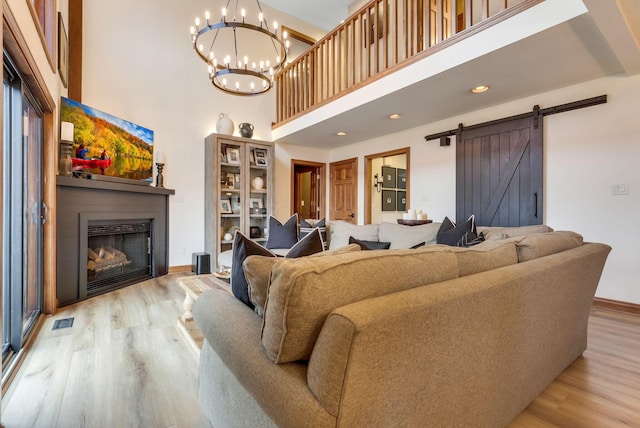 living room featuring a towering ceiling, a barn door, light hardwood / wood-style floors, and a notable chandelier