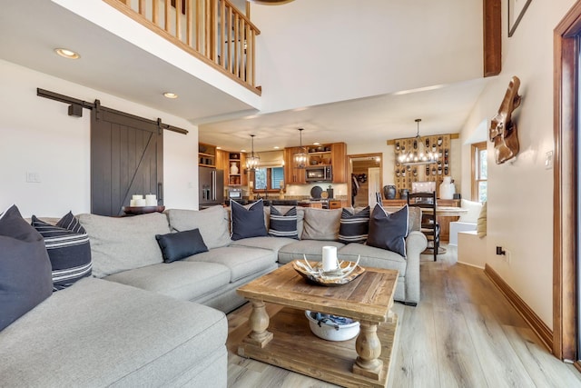 living room featuring an inviting chandelier, a towering ceiling, light hardwood / wood-style flooring, and a barn door