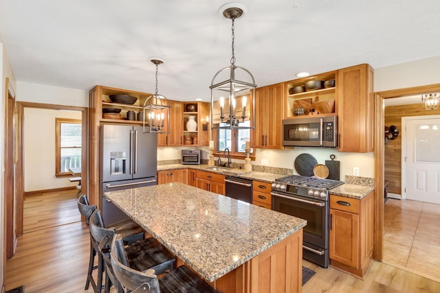 kitchen featuring a kitchen island, appliances with stainless steel finishes, sink, hanging light fixtures, and light stone countertops