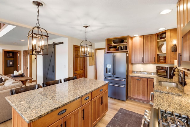 kitchen with a kitchen island, appliances with stainless steel finishes, sink, a barn door, and light stone countertops