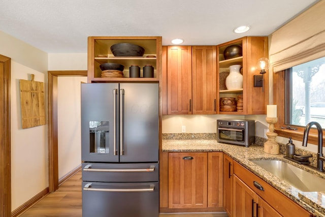 kitchen featuring high end fridge, sink, light stone countertops, and light wood-type flooring