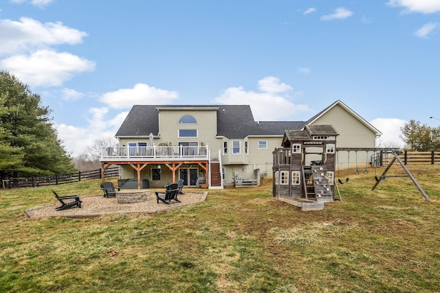 rear view of house with a playground, a wooden deck, a lawn, and a fire pit