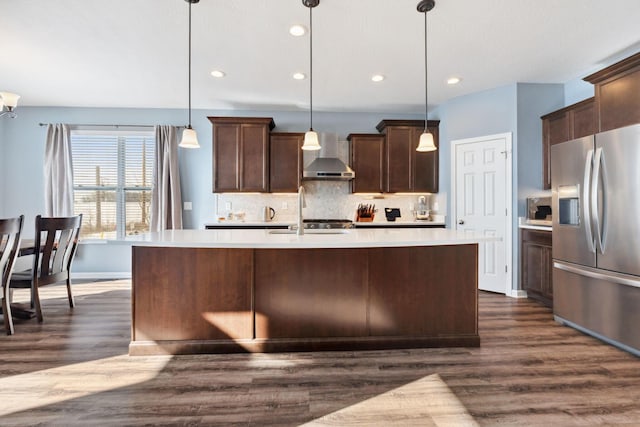 kitchen with stainless steel fridge, tasteful backsplash, wall chimney exhaust hood, light countertops, and a sink