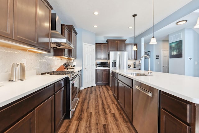 kitchen with dark wood finished floors, appliances with stainless steel finishes, light countertops, wall chimney range hood, and a sink