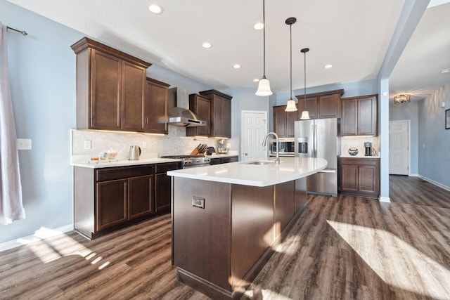 kitchen featuring tasteful backsplash, light countertops, appliances with stainless steel finishes, a sink, and wall chimney exhaust hood