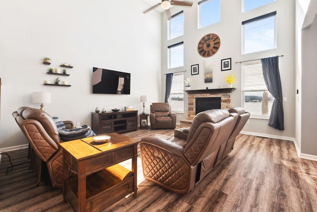 living room with a ceiling fan, baseboards, wood finished floors, and a stone fireplace