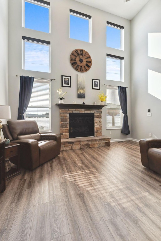 living room featuring a towering ceiling, a stone fireplace, baseboards, and wood finished floors