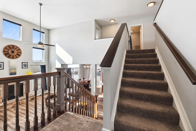 stairway featuring recessed lighting, a towering ceiling, wood finished floors, baseboards, and ceiling fan with notable chandelier