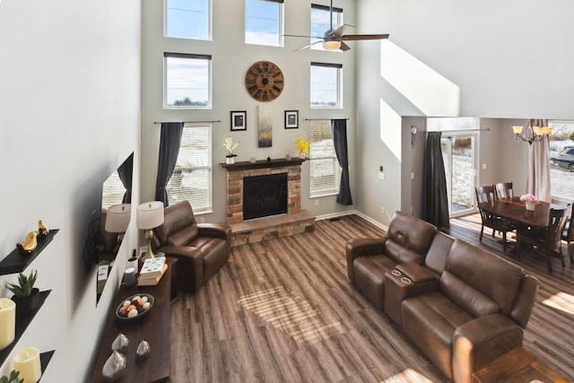 living area featuring a high ceiling, a stone fireplace, baseboards, and ceiling fan with notable chandelier