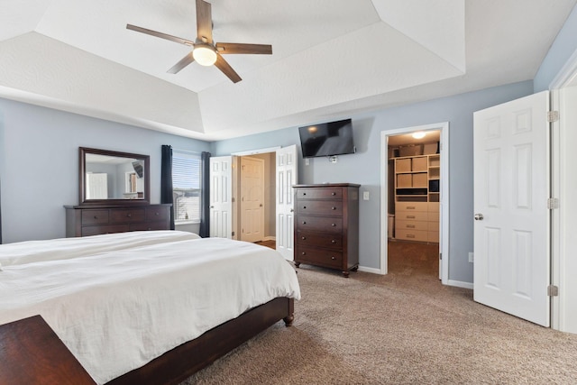 carpeted bedroom with a spacious closet, a tray ceiling, a ceiling fan, and baseboards