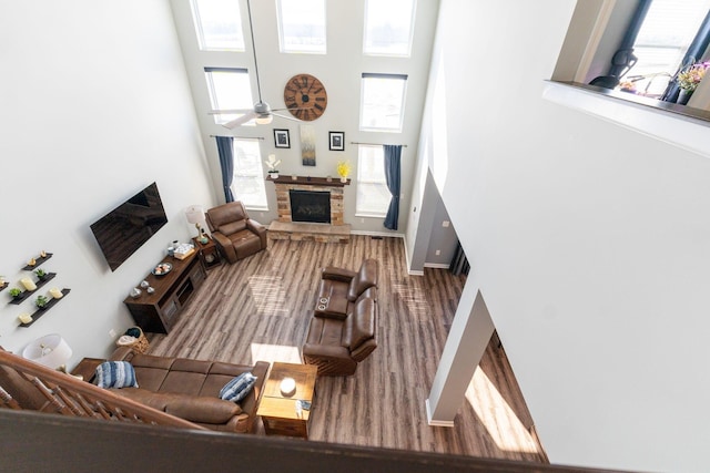 living area with a ceiling fan, baseboards, a stone fireplace, and a high ceiling