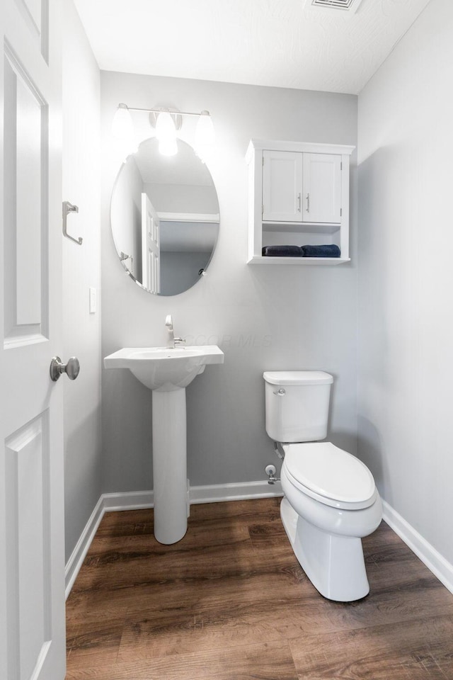 bathroom with toilet, visible vents, baseboards, and wood finished floors